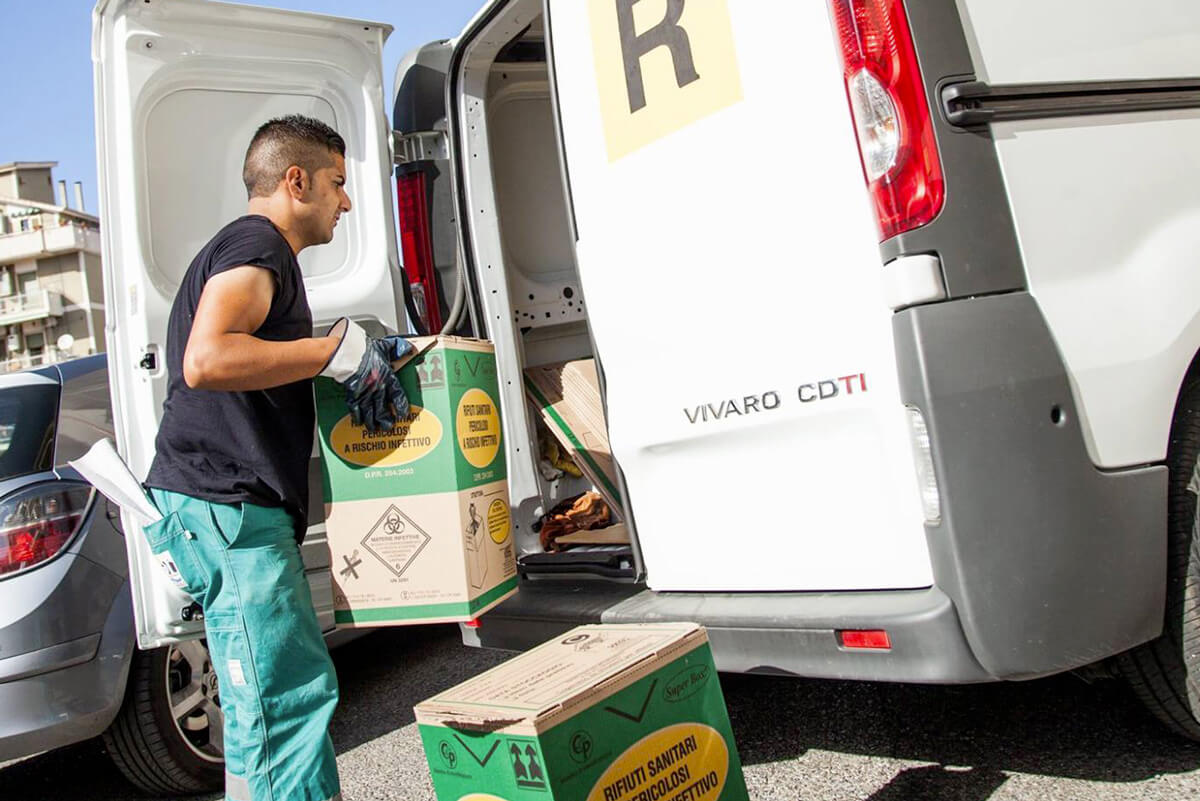 operatore ecoross carica sul furgoncino contenitori dei rifiuti sanitari
